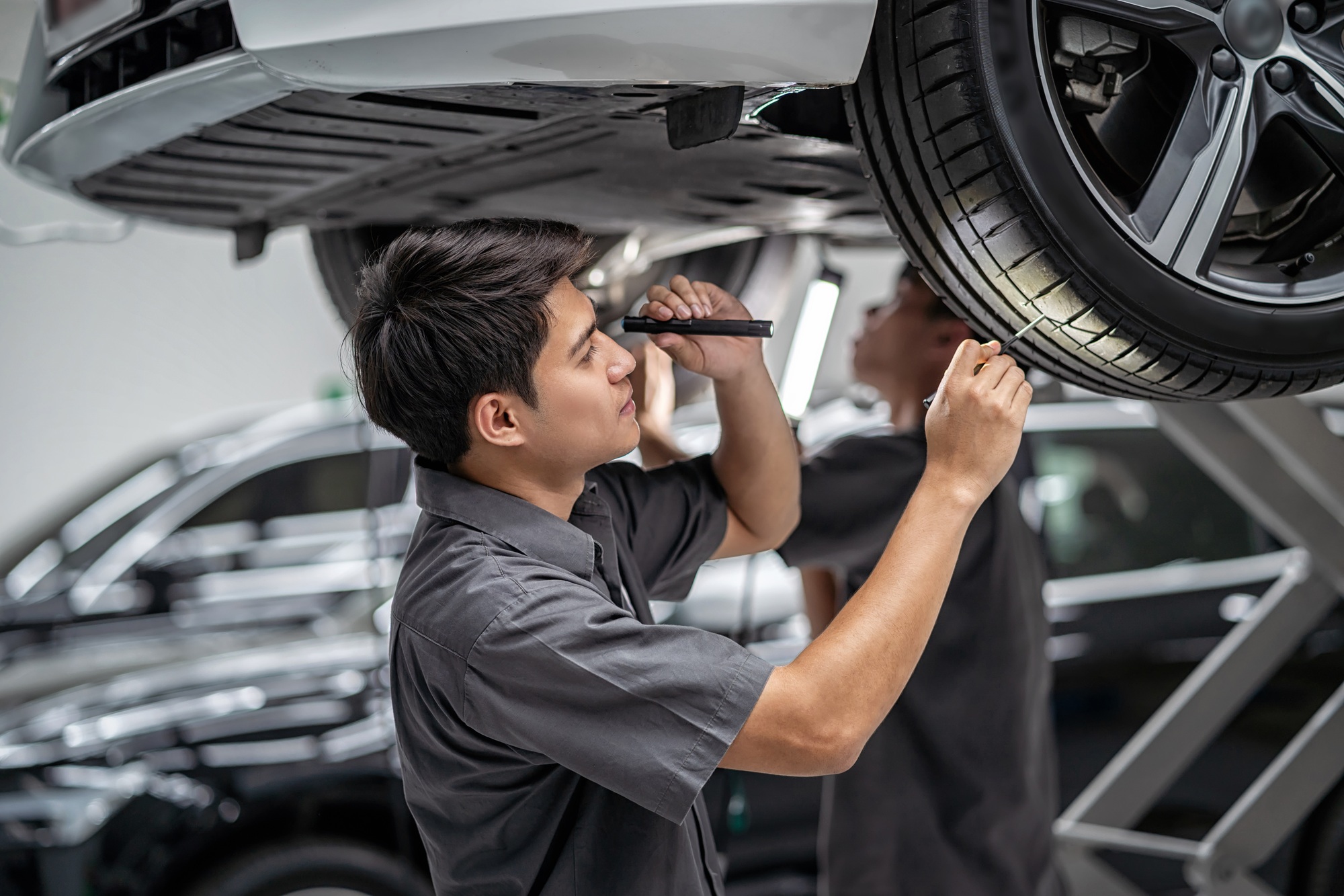 Asian mechanic Checking and torch tire in maintainance service center which is a part of showroom